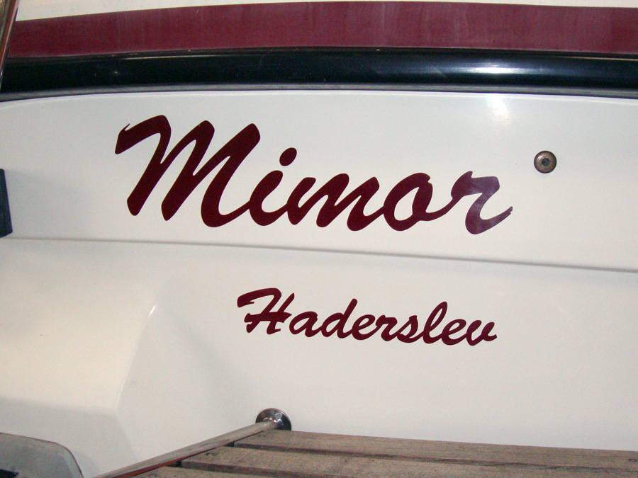 Her ses bådnavnet Mimor og havnenavnet Haderslev. Begge navne til båden er lavet i den samme mørkerøde farve, som vi har valgt at kalde Kardinal Rød.